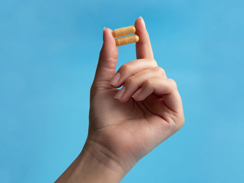 Life Extension, hand holding capsules Two-Per-Day between fingers on a blue background